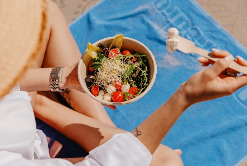 woman sitting on a lounge chair eating a salad, with food service in the beach huts at Vilamoura Beach in the Algarve