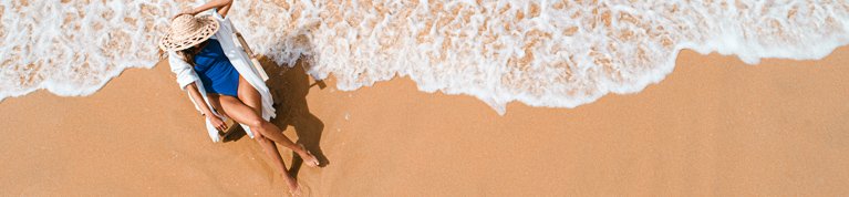 Woman wearing a blue swimsuit and a hat sitting on a chair by the seaside on the beach